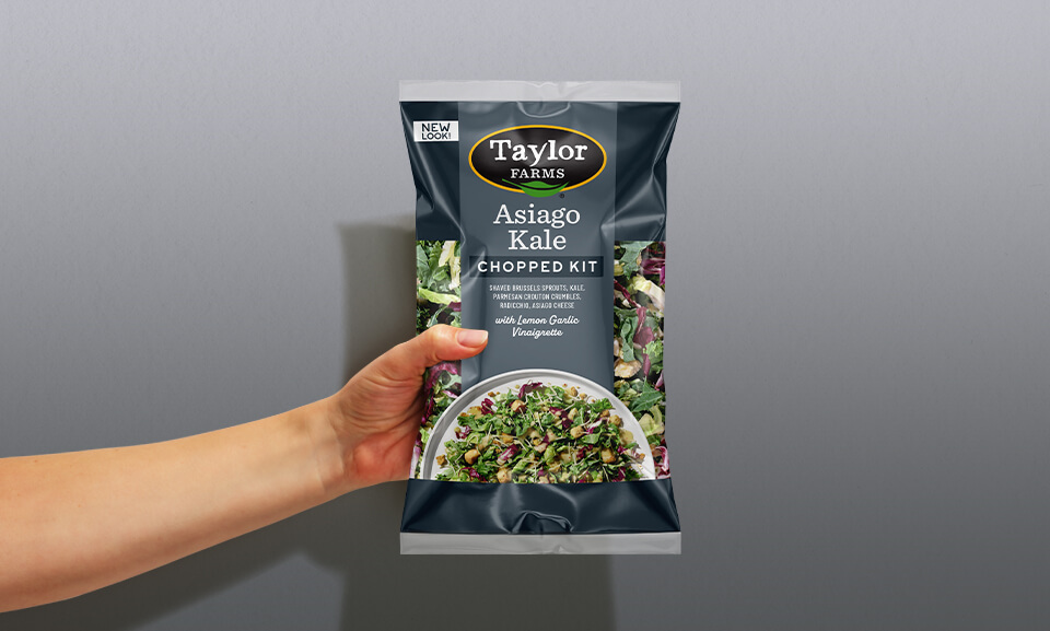 Fresh Asiago kale chopped salad kit held in hand, featuring vibrant greens and flavorful toppings.