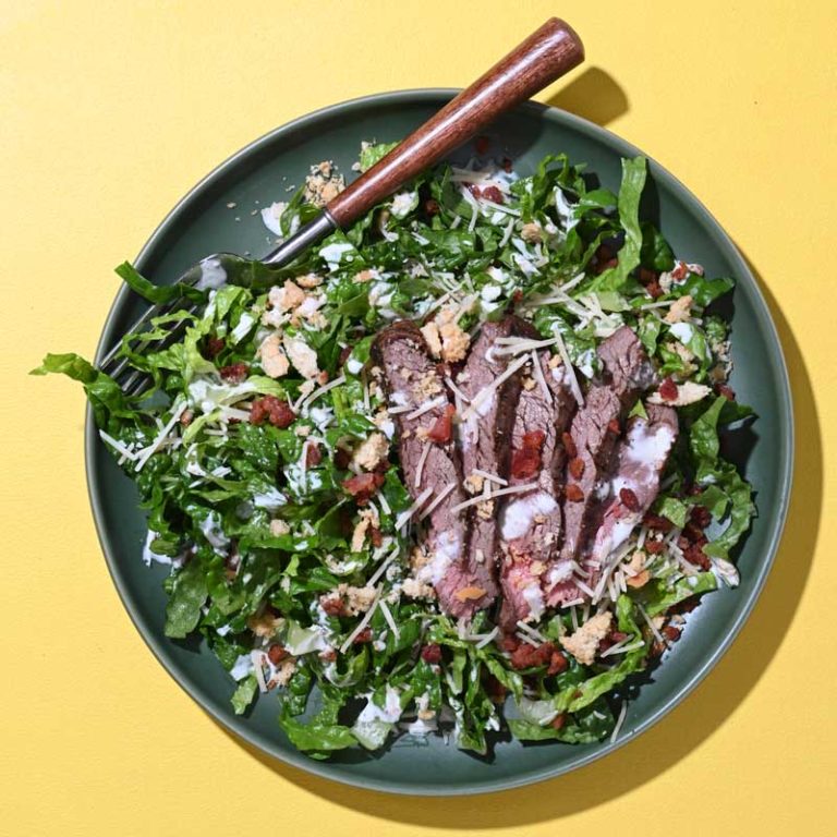 Bacon Caesar chopped salad with fresh greens, crispy bacon, and Caesar dressing garnish.