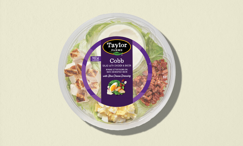 Cobb salad single serve bowl featuring fresh greens, avocado, eggs, bacon, and dressing on a colorful background.