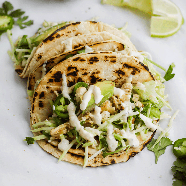 Roasted garlic green goddess tacos topped with fresh vegetables and herbs, served on a wooden table.