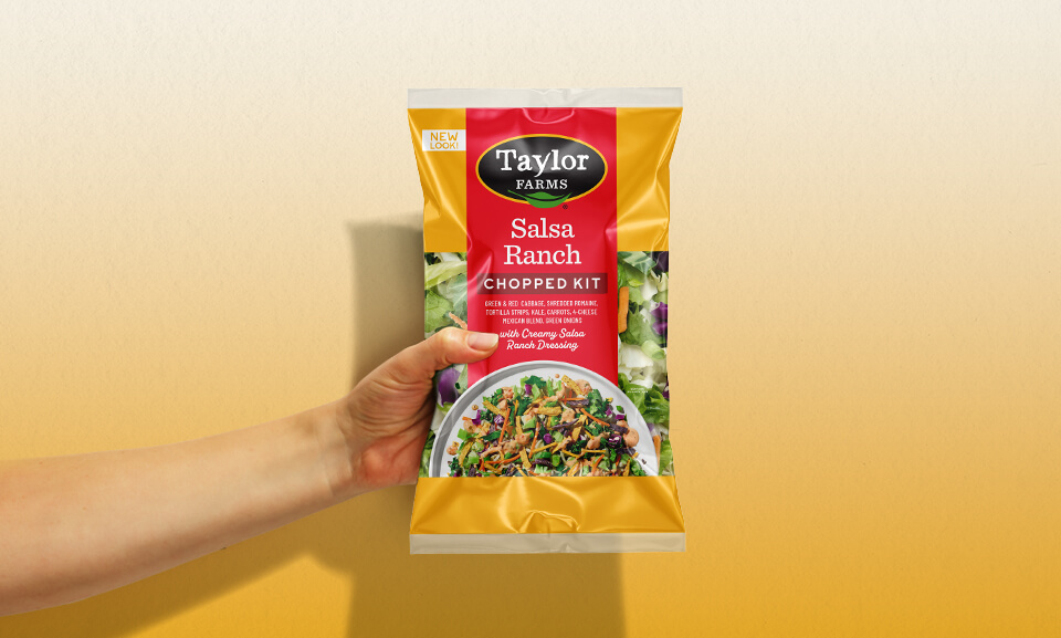 Hand holding a plate of Taylor Farms Salsa Ranch Chopped Kit with vibrant vegetables and dressing.