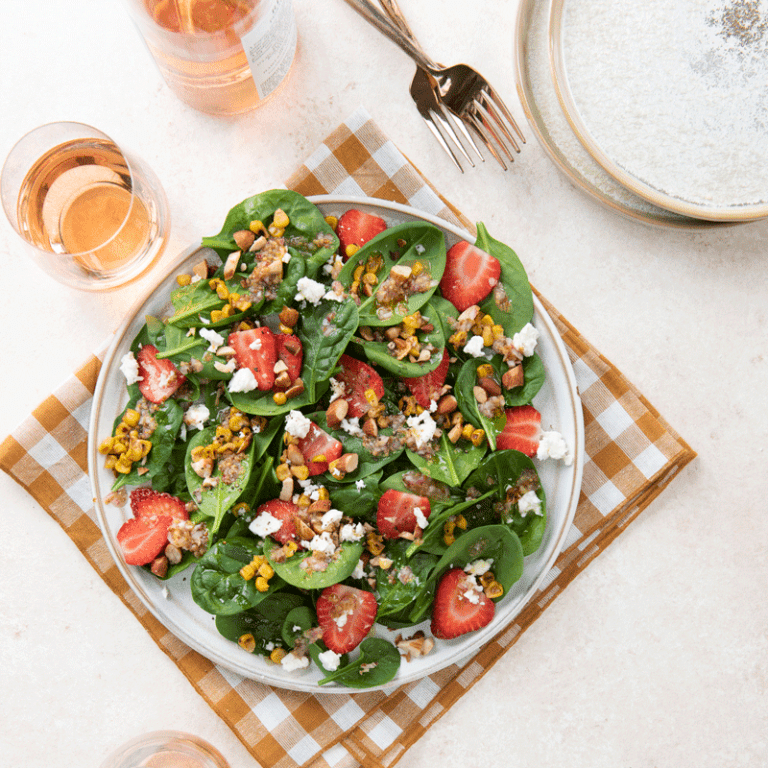 Fresh summer spinach salad topped with grilled corn, juicy strawberries, and crumbled feta cheese.