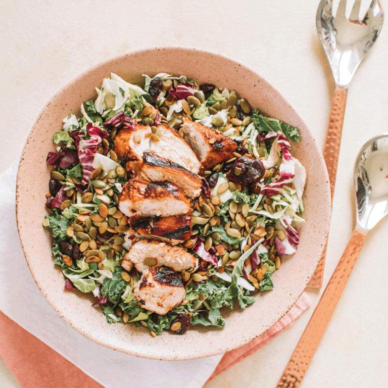 Sweet kale salad topped with balsamic herb chicken, showcasing a healthy and colorful meal option.