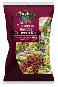The Maple Bourbon Bacon Chopped Salad kit package, showing chopped romaine lettuce, broccoli, cabbage, and carrots, which are topped with golden honey almonds, smoky bacon, grilled chicken, and Maple Bourbon Vinaigrette dressing.