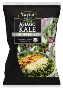 The Asiago Kale Chopped Salad kit package, showing chopped kale, shaved Brussels sprouts, and radicchio topped with Asiago cheese, Parmesan garlic crouton crumbles, and lemon garlic dressing.