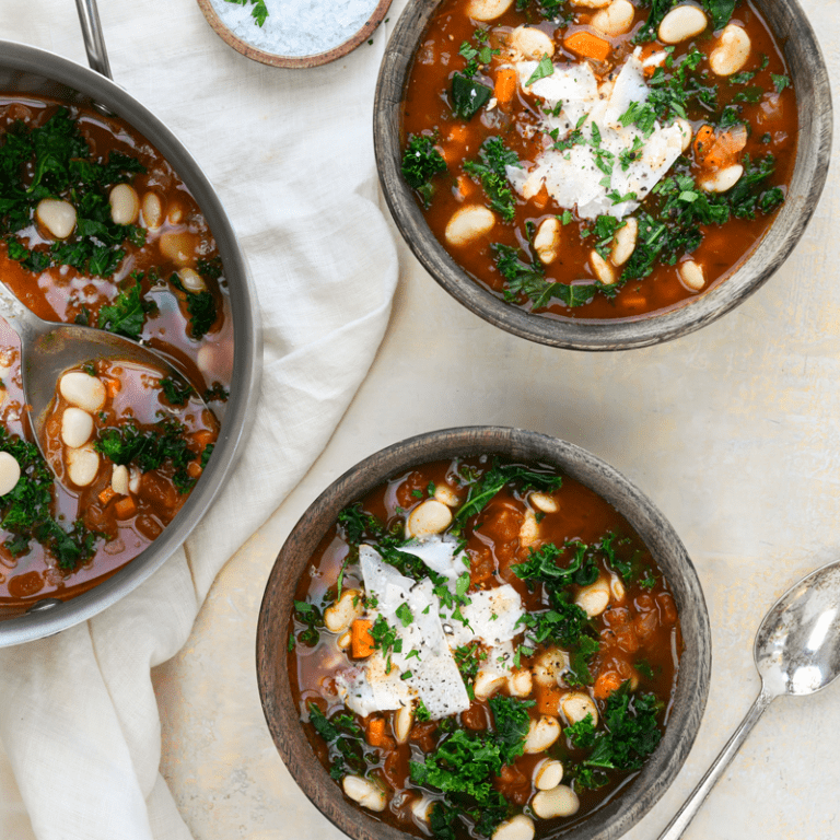Hearty tomato, white bean, and kale soup garnished with fresh herbs in a bowl.