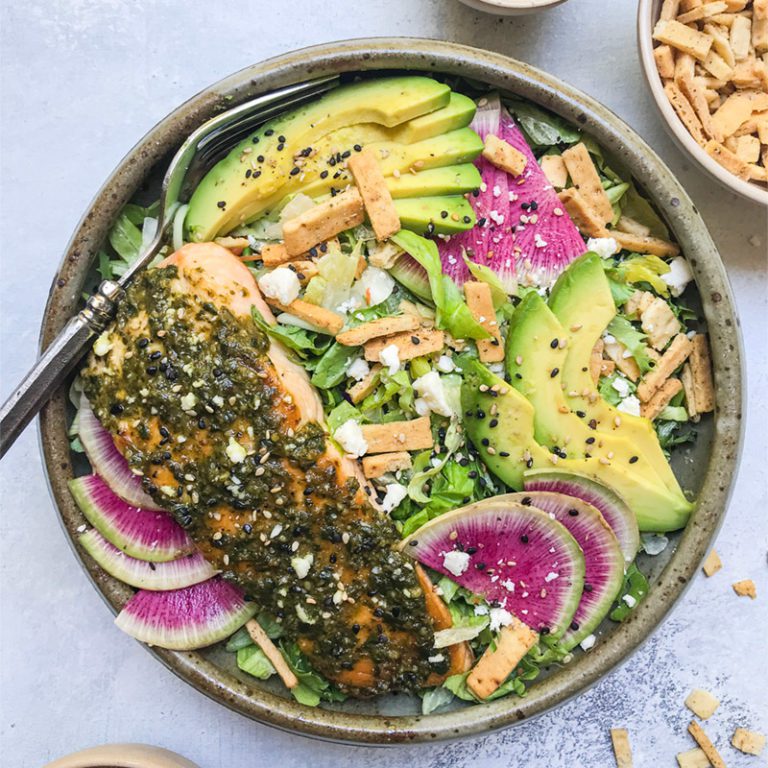 Sliced pesto salmon served on a plate, garnished with fresh herbs and lemon wedges.