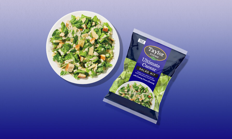 Fresh Ultimate Caesar Salad Kit displayed on a white plate with romaine, croutons, parmesan, and dressing.