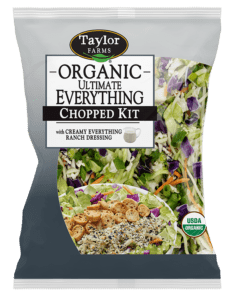 The Organic Ultimate Everything Chopped Salad kit package, showing green romaine lettuce, red cabbage, shredded broccoli, and carrots topped with smoked white cheddar, bagel chips, and Everything Ranch dressing.