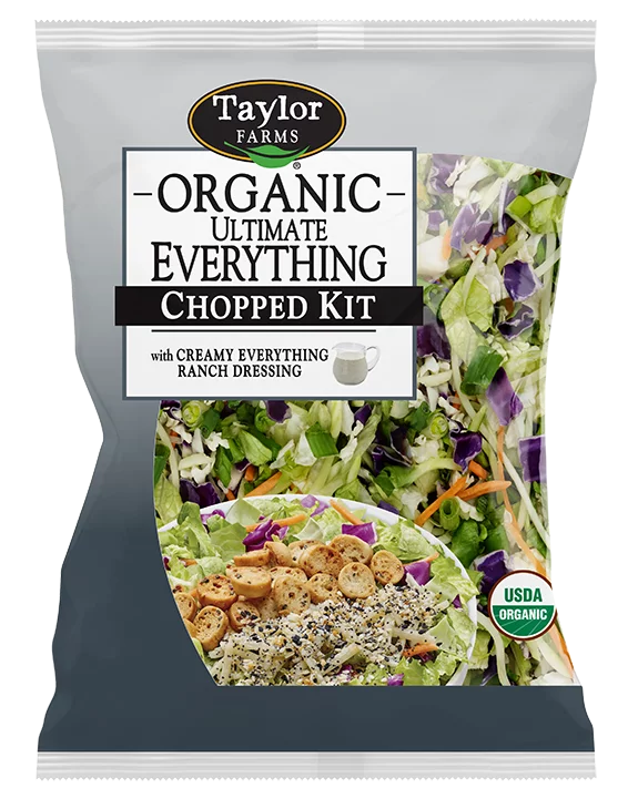 The Organic Ultimate Everything Chopped Salad kit package, showing green romaine lettuce, red cabbage, shredded broccoli, and carrots topped with smoked white cheddar, bagel chips, and Everything Ranch dressing.