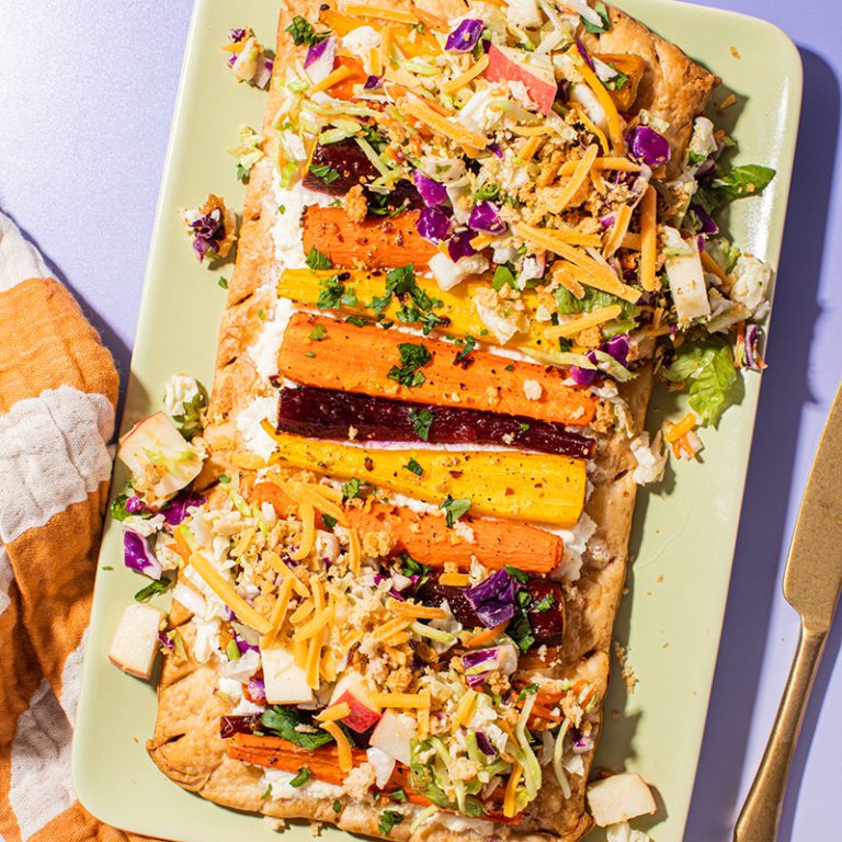 Maple Dijon Crunch Carrot Tart topped with crunchy nuts and herbs on a rustic wooden table.