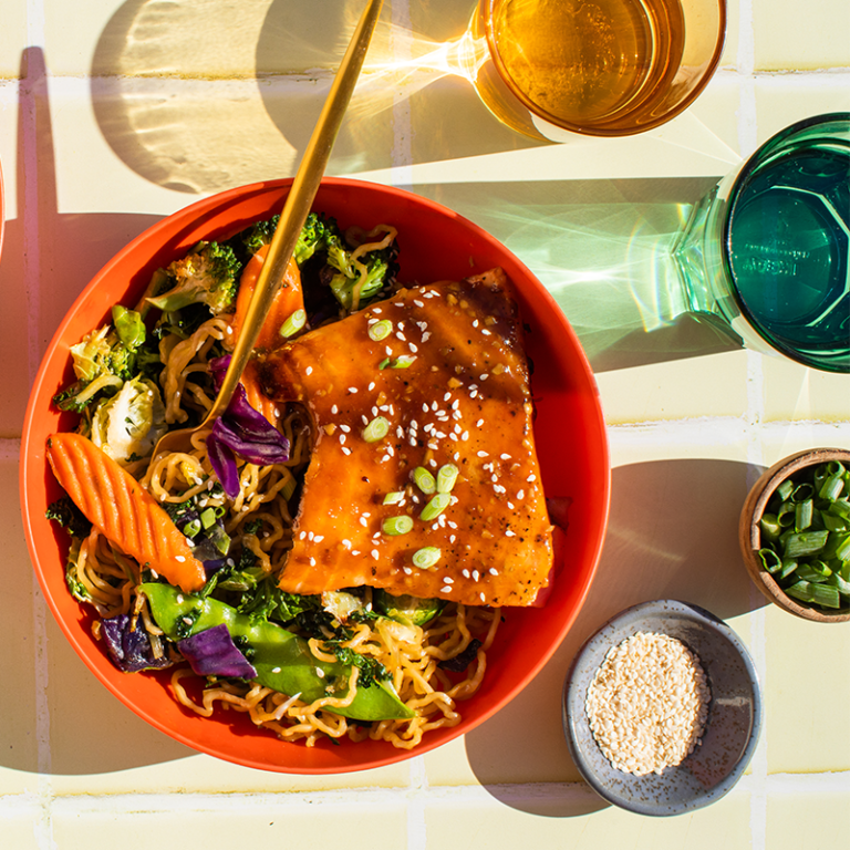 Teriyaki noodles topped with colorful vegetables and meat, served in a vibrant bowl.