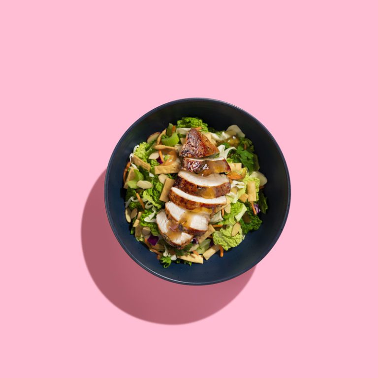 Asian teriyaki chicken salad with mixed greens, sesame seeds, and colorful vegetables in a vibrant bowl.