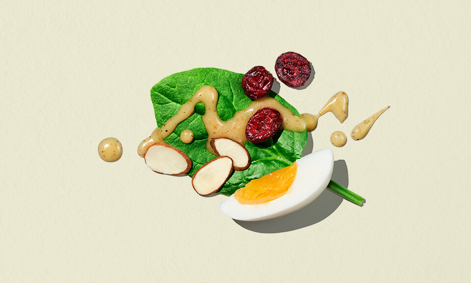 Single-serve spinach salad with Dijon dressing in a clear bowl, showcasing vibrant greens and fresh ingredients.