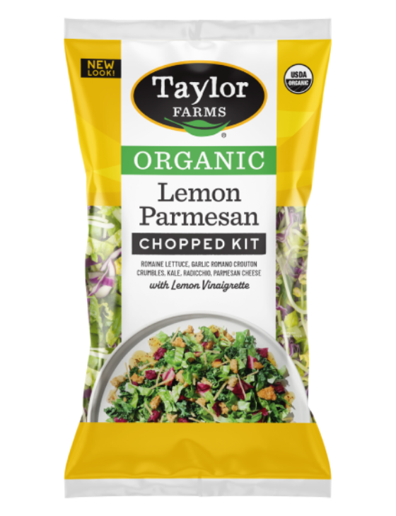 Taylor Farms Organic Lemon Parmesan Chopped Salad package, next to an open tortilla on a plate with the Lemon Parmesan Salad, topped with sliced avocado and a creamy sauce.