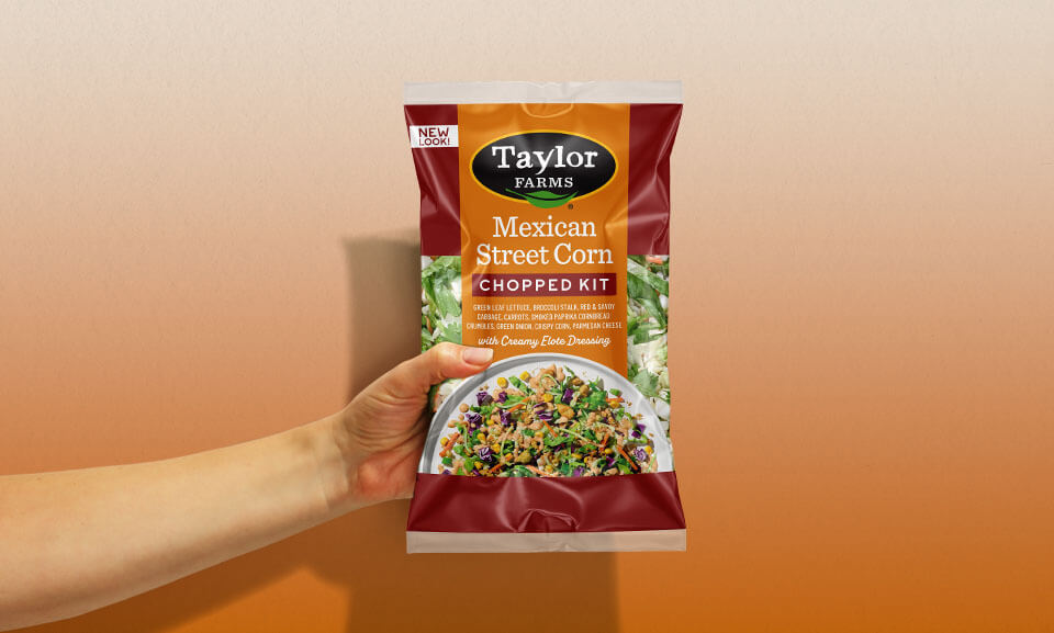 Hand holding a bag of Taylor Farms Mexican Street Corn Chopped Kit, showcasing fresh ingredients for a flavorful meal.