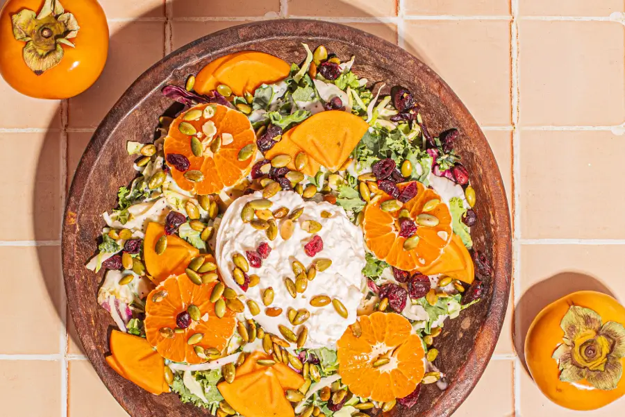 Harvest salad with persimmons, burrata cheese, and fresh greens, garnished with nuts and a vinaigrette dressing.