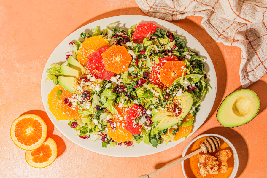 Taylor Farms winter citrus avocado salad in a bowl surrounded by oranges, avocado, and honey