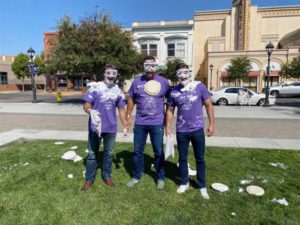 three men in purple shirts with pie on faces