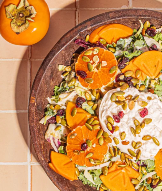 Persimmon and burrata harvest salad topped with fresh greens, nuts, and a light vinaigrette dressing.
