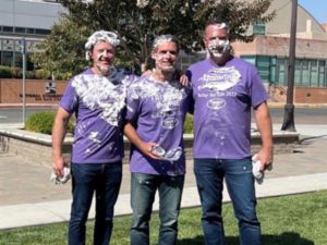 three men in purple shirts with pie on faces