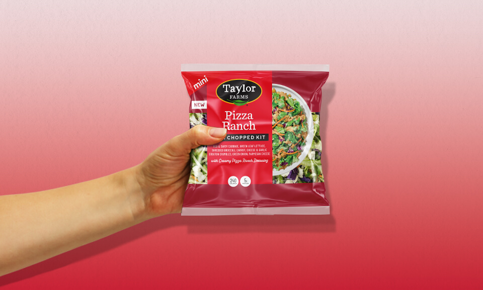 Hand holding a Pizza Ranch Mini Chopped Kit bag, showcasing fresh salad ingredients and vibrant packaging.