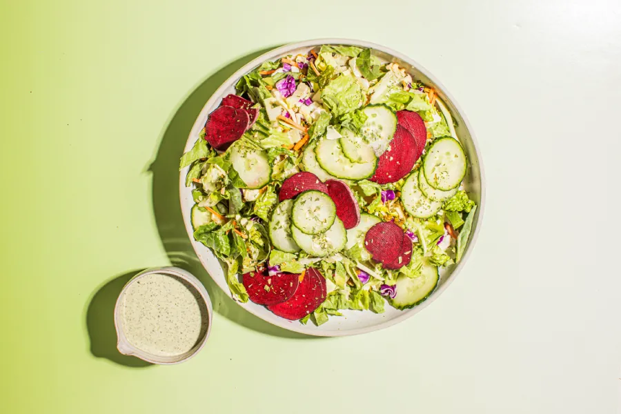 Bowl of Taylor Farms Beet & Cucumber Green Goddess Salad with a side of dressing