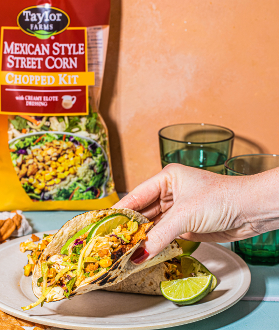 Taylor Farms Mexican Street Corn Tacos being picked up by a hand with a package in the background