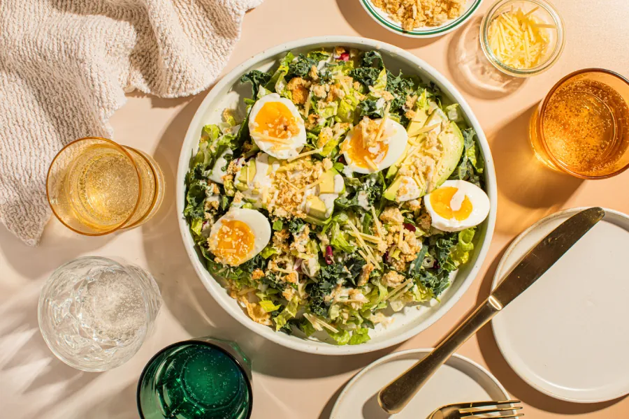 Taylor Farms Kale Caesar with Jammy Eggs in a bowl surrounded by glasses