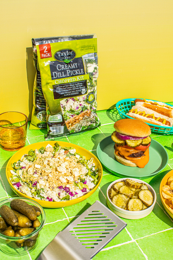Grilled food featuring dill pickles and fresh vegetables in an outdoor dining setting.