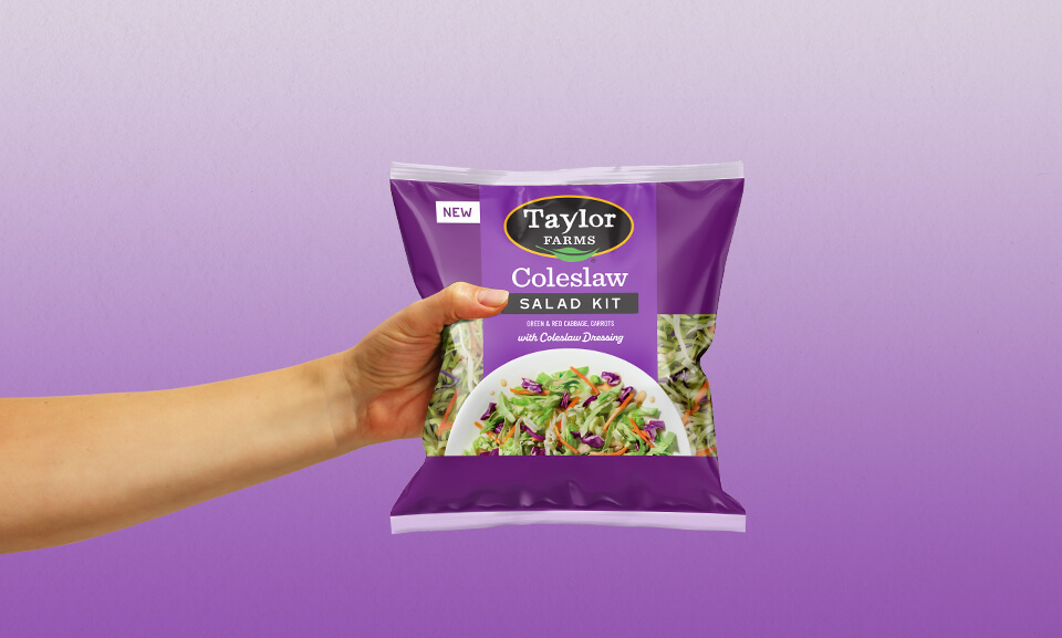 Hand holding a bag of Taylor Farms Coleslaw Salad Kit, showcasing fresh ingredients for quick and healthy meals.