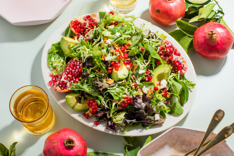 Pomegranate, avocado, and apple feta salad garnished with fresh greens, showcasing vibrant colors and healthy ingredients.