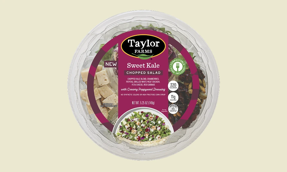 Packaged sweet kale chopped salad with cranberries, feta, grilled white chicken, and creamy poppyseed dressing in a clear compostable bowl.