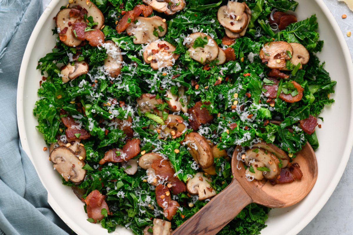 Kale sauté with mushrooms and crispy bacon served in a skillet, showcasing a delicious, healthy dish.