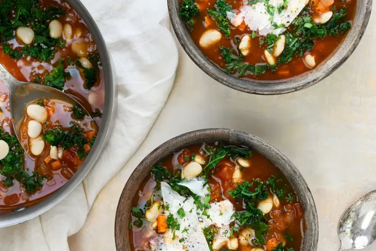 Hearty tomato, white bean, and kale soup garnished with fresh herbs in a bowl.